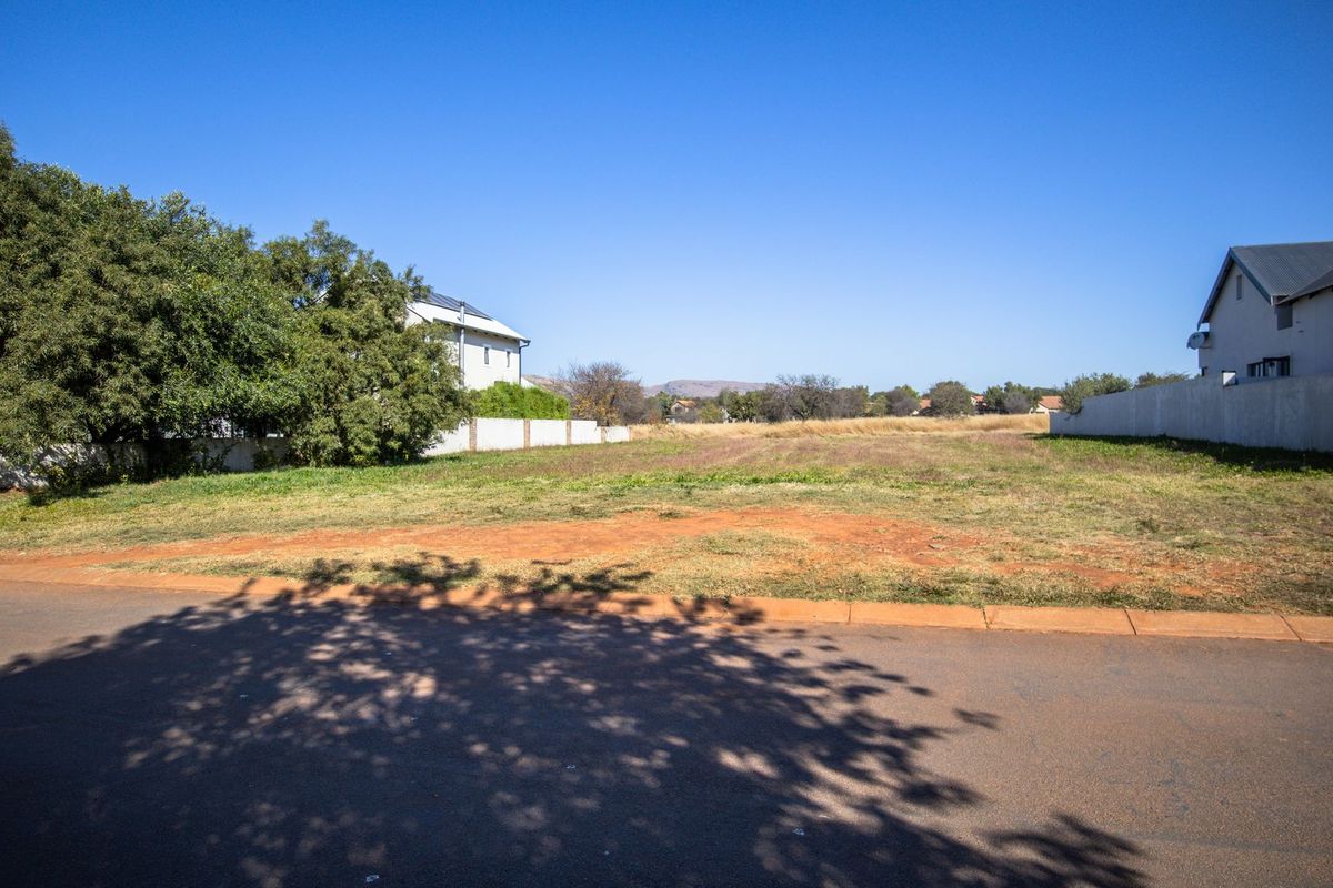 A vacant residential plot situated in a developed neighborhood, featuring level ground, boundary walls, and direct access to a paved street.