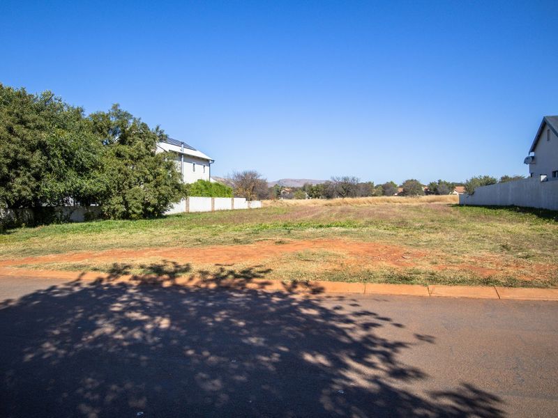 A vacant residential plot situated in a developed neighborhood, featuring level ground, boundary walls, and direct access to a paved street.