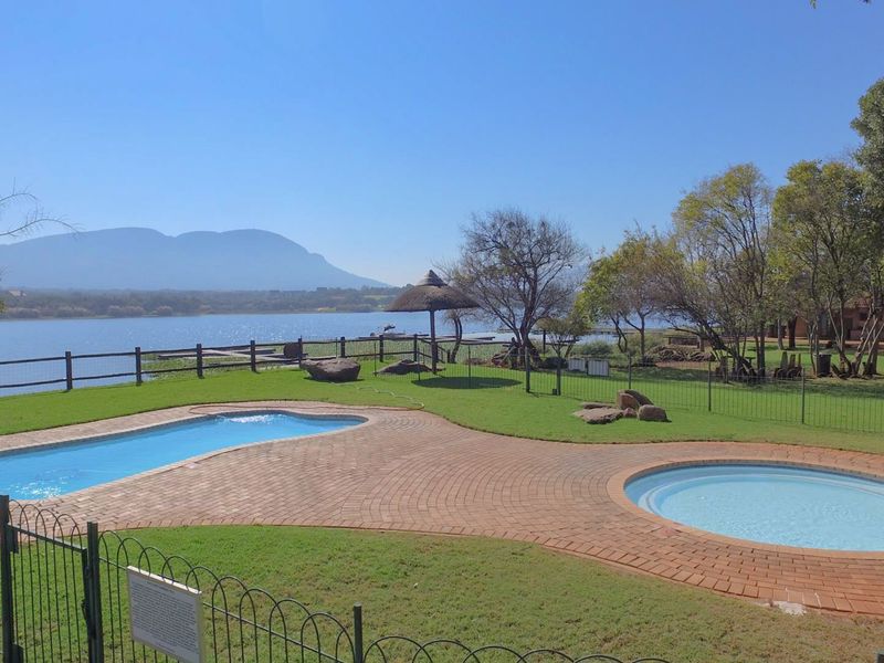 Outdoor pool area featuring two swimming pools, brick paving, and landscaped garden with scenic lake and mountain views.