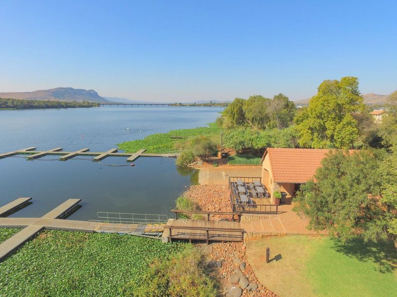 Aerial view of a waterfront property featuring boat jetties, a paved patio area, and a structure with a tiled roof overlooking the lake.