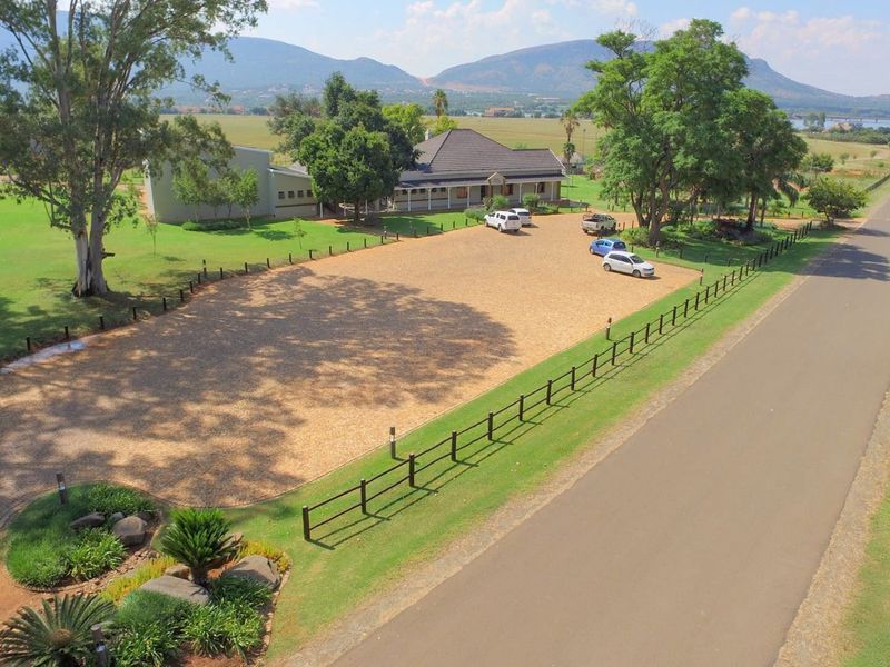 Aerial view of a spacious residential property featuring a large paved driveway, well-maintained garden, and perimeter fencing with scenic mountain views.