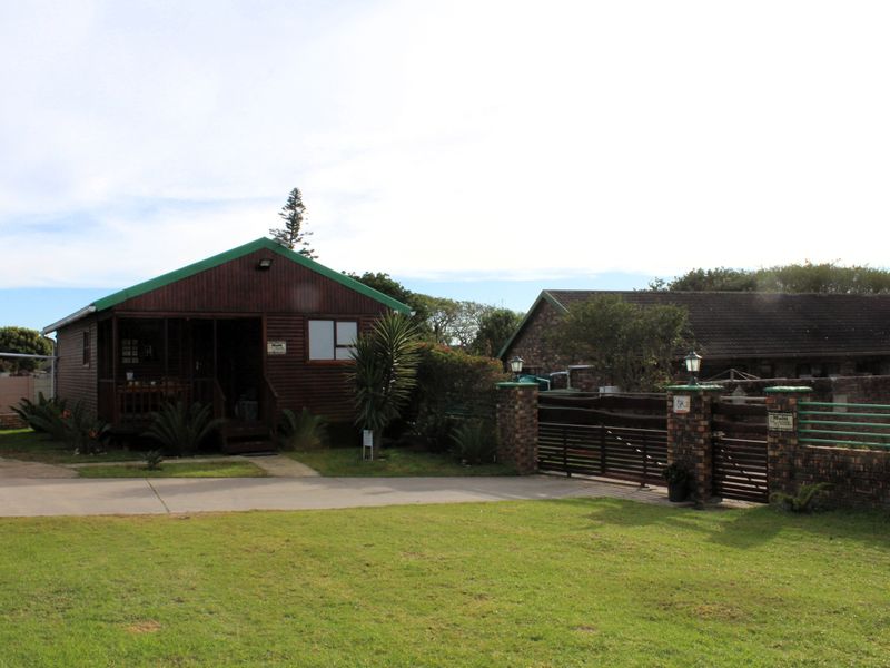 Front view of a timber-clad house featuring a covered porch, concrete driveway, and a brick boundary wall with a metal gate.