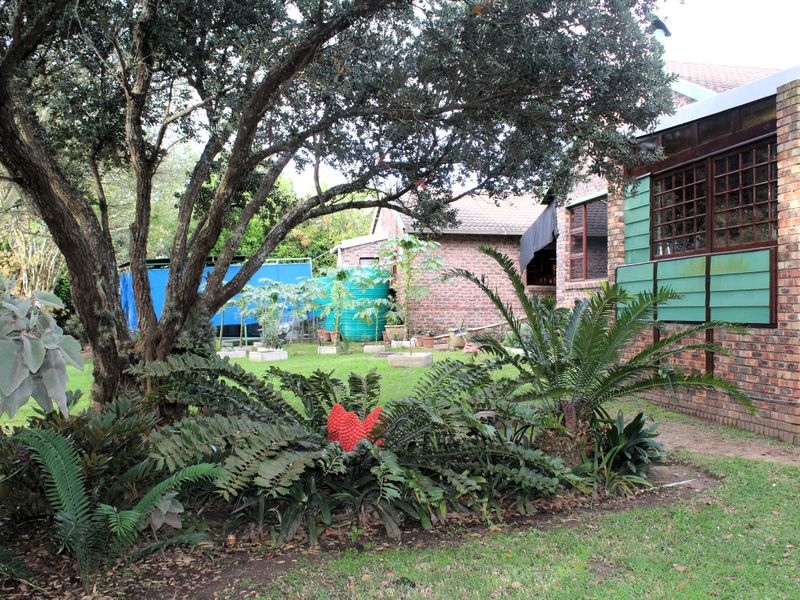 A view of the rear garden featuring established trees, landscaped beds, and the brick exterior of the house with timber-framed windows.