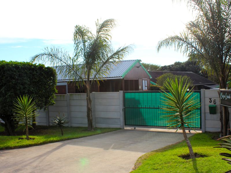 Front view of the property featuring a concrete driveway, secure sliding gate, and precast boundary wall with established garden landscaping.