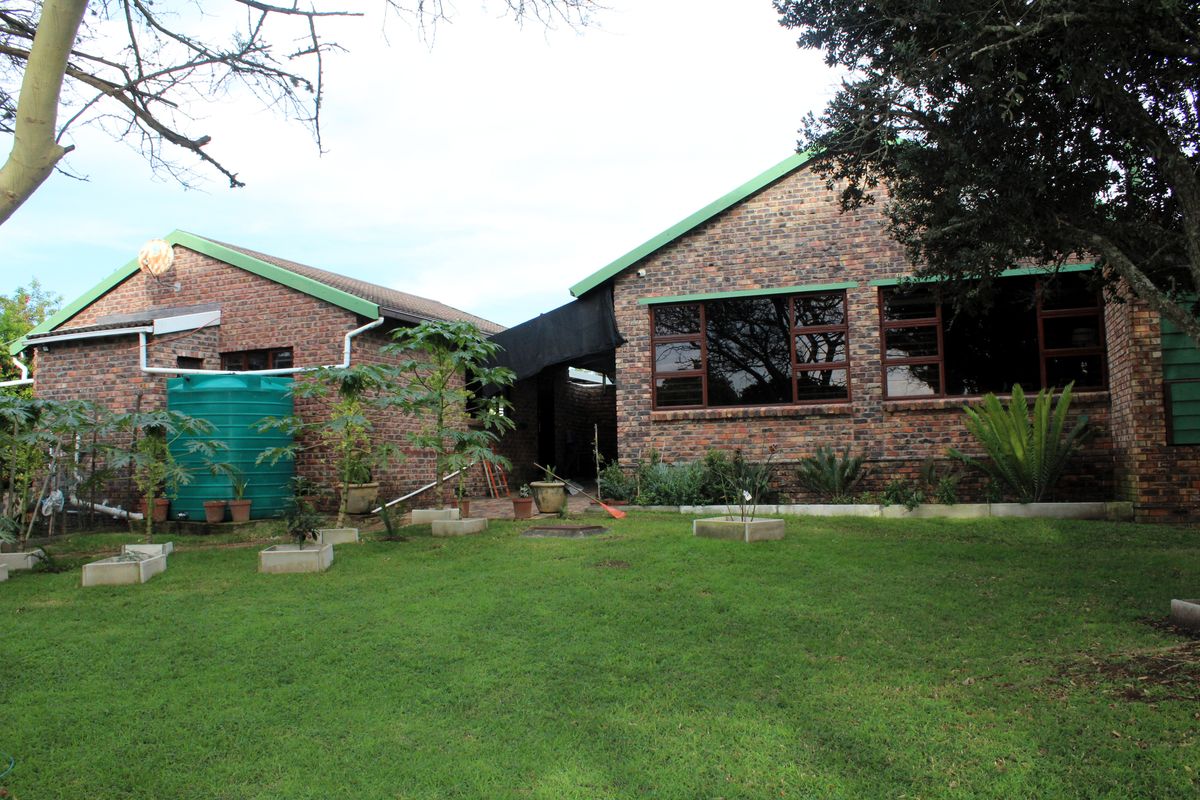 Rear view of a face brick house featuring a large lawn, established garden, and a water storage tank.