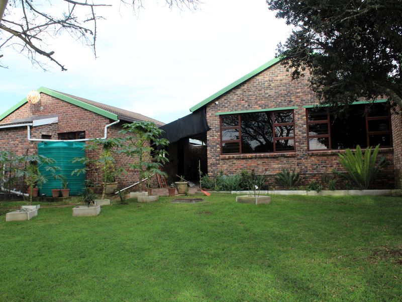 Rear view of a face brick house featuring a large lawn, established garden, and a water storage tank.
