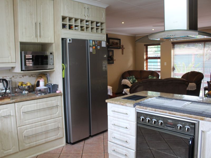 Open-plan kitchen featuring light wood cabinetry, granite countertops, and a central island with a built-in oven, flowing into a comfortable living area.