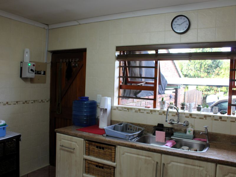 A functional kitchen area featuring a double bowl stainless steel sink, laminate countertops, tiled backsplash, and built-in cabinetry with louvre windows.
