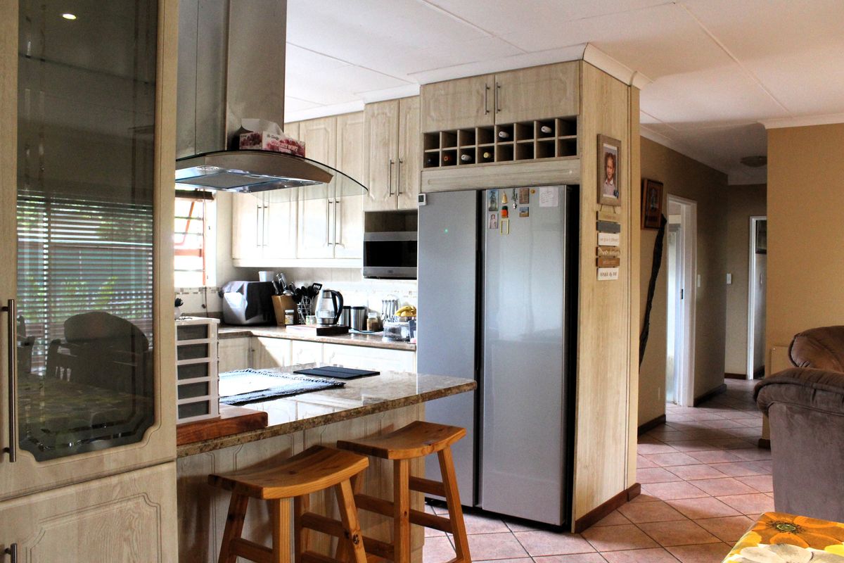 A functional kitchen featuring light wood cabinetry, granite countertops, a built-in wine rack, and an extractor fan, with tiled flooring throughout.