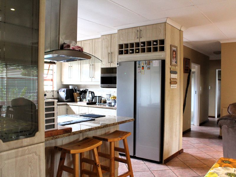 A functional kitchen featuring light wood cabinetry, granite countertops, a built-in wine rack, and an extractor fan, with tiled flooring throughout.