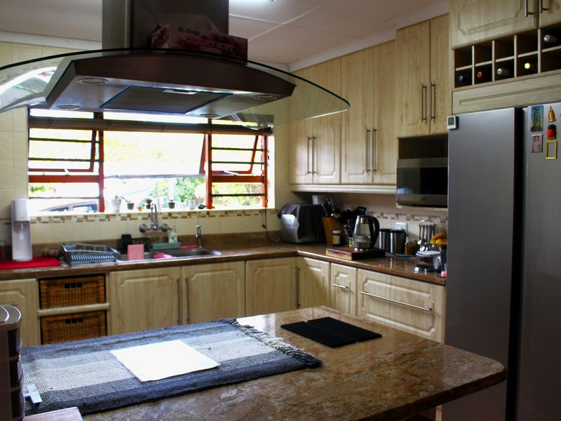 A functional kitchen featuring light wood cabinetry, granite countertops, a central island, and a modern glass extractor fan over the sink area.