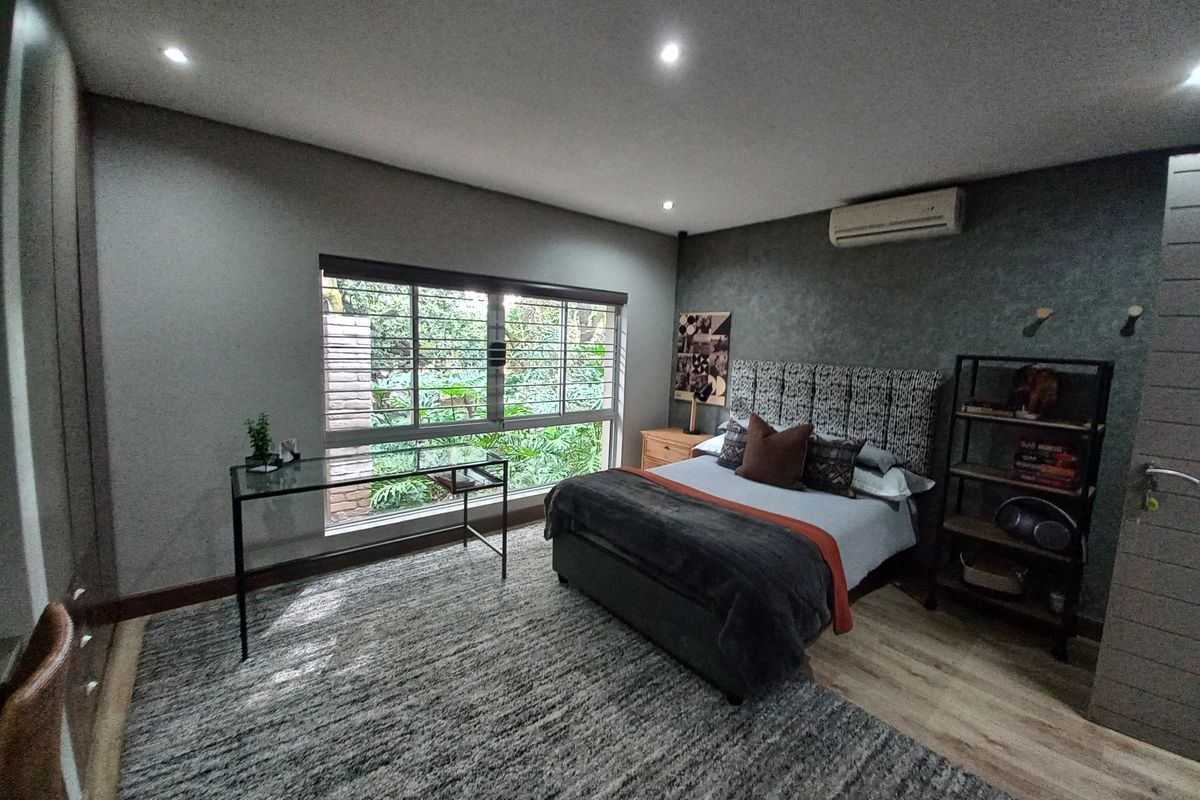 A well-maintained bedroom featuring recessed lighting, a split-system air conditioner, built-in cupboards, and large windows overlooking a garden.