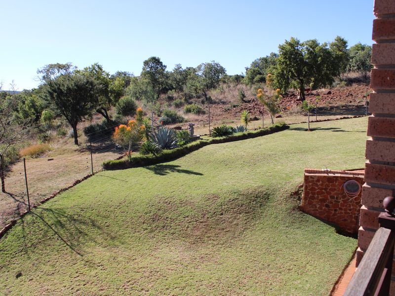 A spacious, well-maintained garden area featuring a manicured lawn, stone-clad retaining wall, and established landscaping with a natural bushveld backdrop.