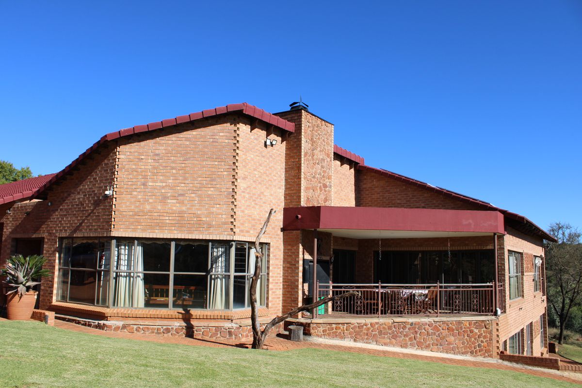 Rear view of a brick house featuring a covered patio, stone-clad chimney, and large bay windows overlooking a landscaped garden.