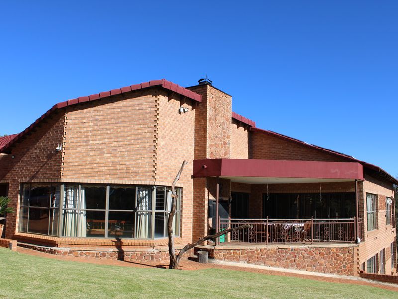 Rear view of a brick house featuring a covered patio, stone-clad chimney, and large bay windows overlooking a landscaped garden.