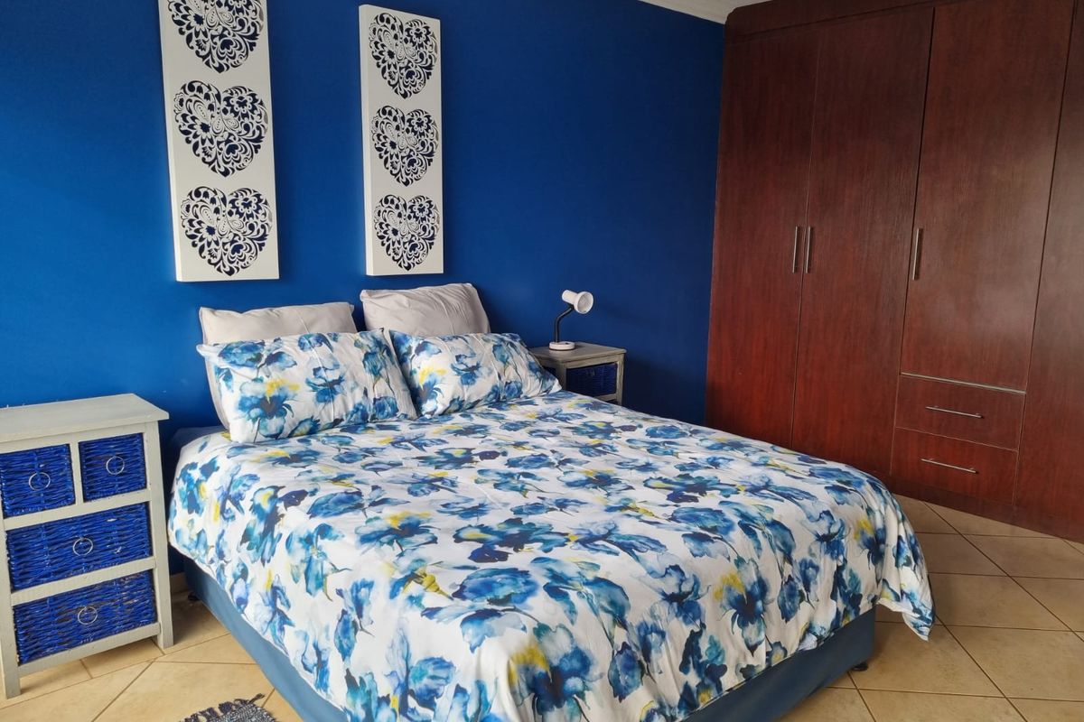 A bedroom featuring dark wood built-in cupboards, vibrant blue accent wall, and neutral tiled flooring.