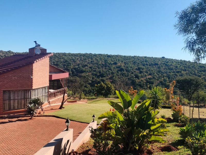 A well-maintained brick house featuring a paved driveway, landscaped garden, and expansive views of the surrounding natural landscape.