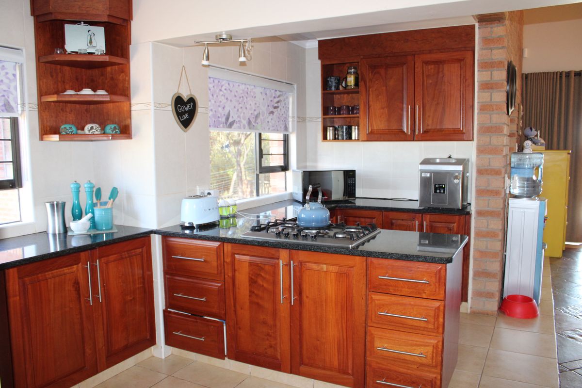 A functional kitchen featuring warm wooden cabinetry, granite countertops, a gas hob, and an exposed brick feature wall, offering a classic aesthetic.