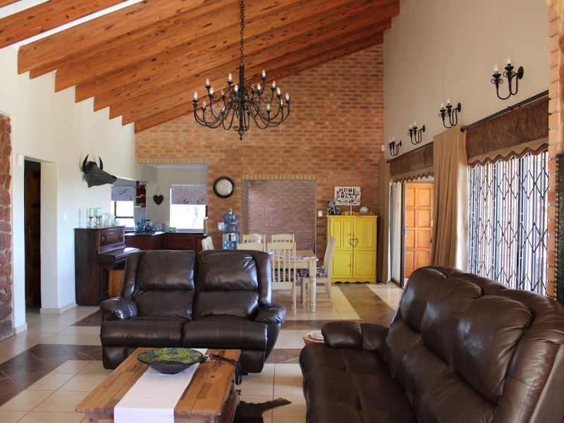 Spacious open-plan living and dining area featuring high vaulted timber ceilings, exposed brickwork, stone feature walls, and large windows with security gates.