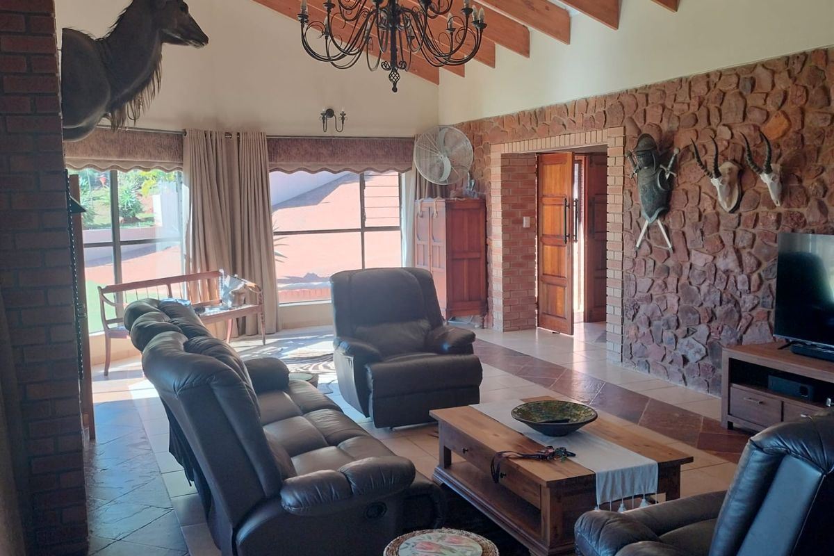 Spacious living room featuring a vaulted ceiling with exposed timber beams, a prominent stone feature wall, and a brick fireplace, offering a rustic aesthetic.
