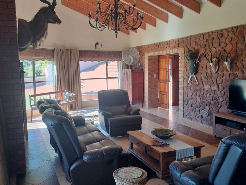 Spacious living room featuring a vaulted ceiling with exposed timber beams, a prominent stone feature wall, and a brick fireplace, offering a rustic aesthetic.