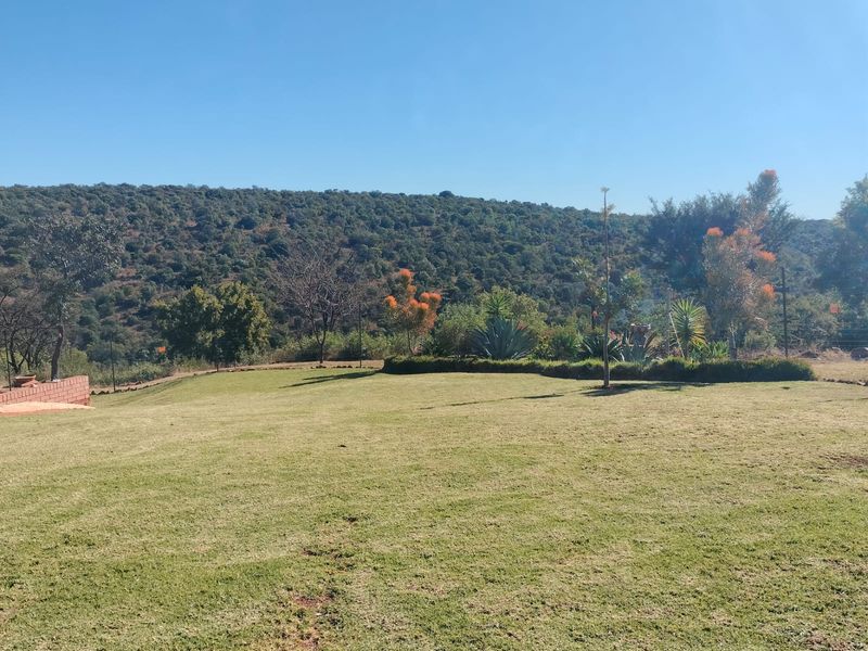 A wide-angle view of a well-maintained lawn and landscaped garden area, featuring a scenic backdrop of rolling hills and natural vegetation.