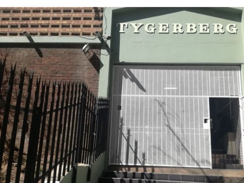 Front entrance of the Tygerberg complex featuring a secure metal gate, brick facade, and tiled steps.