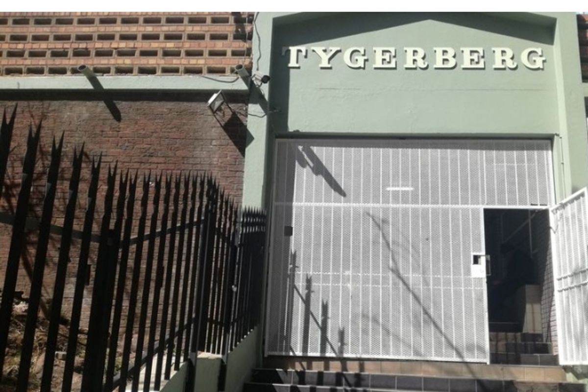 Front entrance of the Tygerberg complex featuring a secure metal gate, brick facade, and tiled steps.
