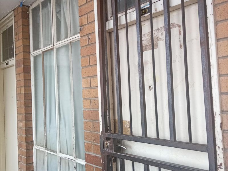 Exterior entrance featuring a brick facade, a metal security gate, and multi-pane windows.