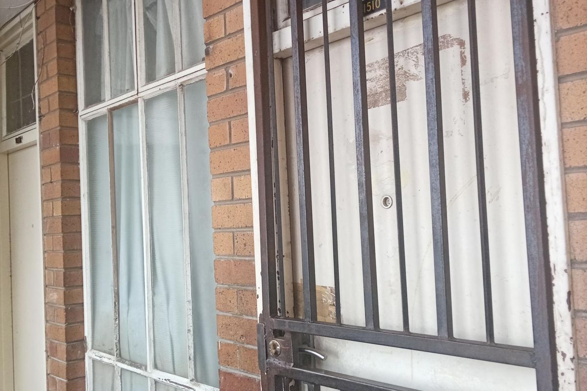 Exterior entrance featuring a brick facade, a metal security gate, and multi-pane windows.