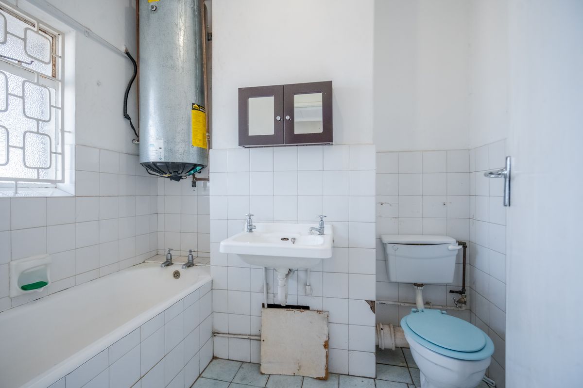 A dated bathroom featuring a bathtub, wall-mounted water heater, basin, and toilet, requiring renovation to update the finishes and fixtures.