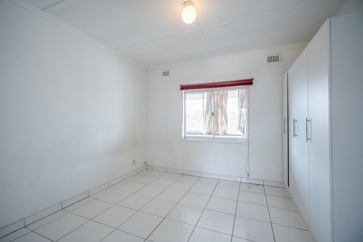 A bright, empty bedroom featuring white tiled flooring, built-in cupboards, and a central ceiling light fixture.