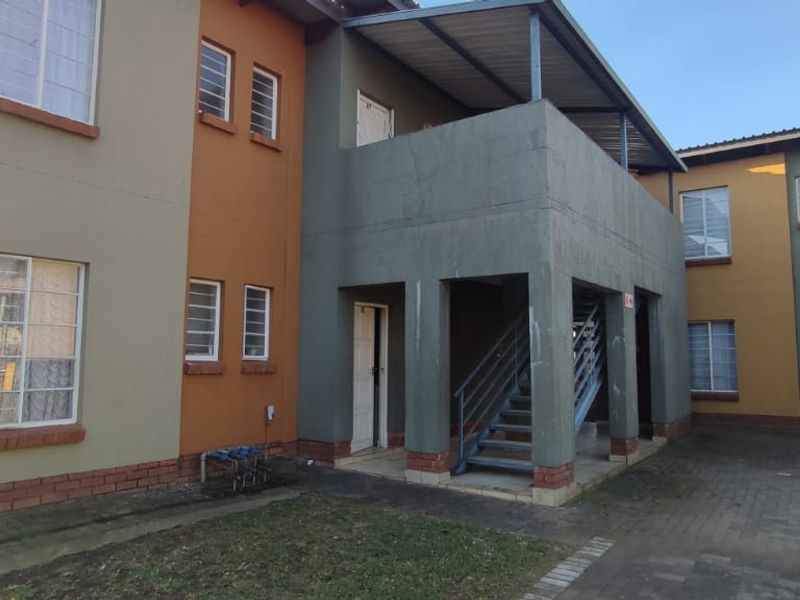 Exterior view of a multi-story townhouse complex featuring paved driveway access, external staircases, and a multi-toned facade with brick detailing.