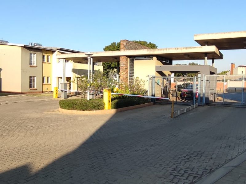 The entrance to the townhouse complex features a secure boom gate, paved driveway, and modern concrete canopy structure.