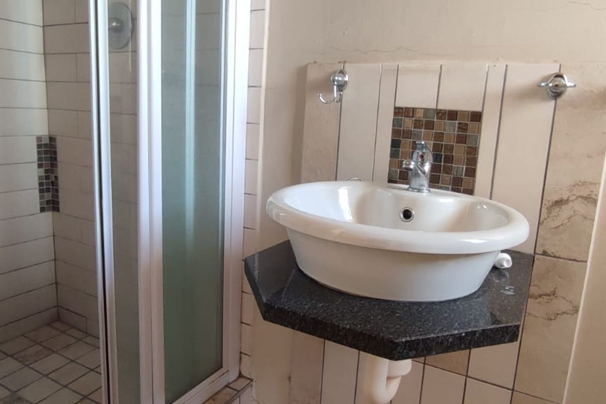 A functional bathroom featuring a shower enclosure, a vessel sink mounted on a granite vanity top, and decorative tiled splashback detailing.