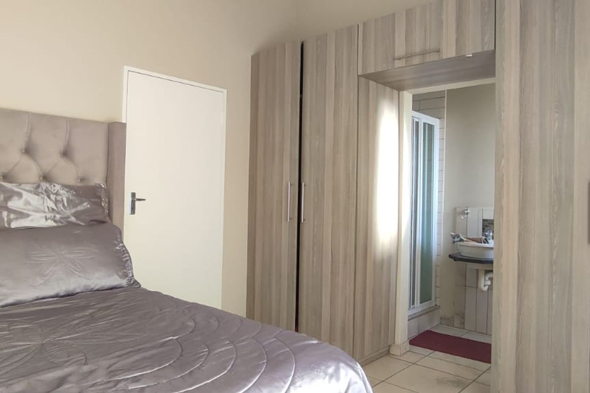 A well-maintained bedroom featuring extensive built-in cupboards and direct access to an en-suite bathroom with tiled flooring.
