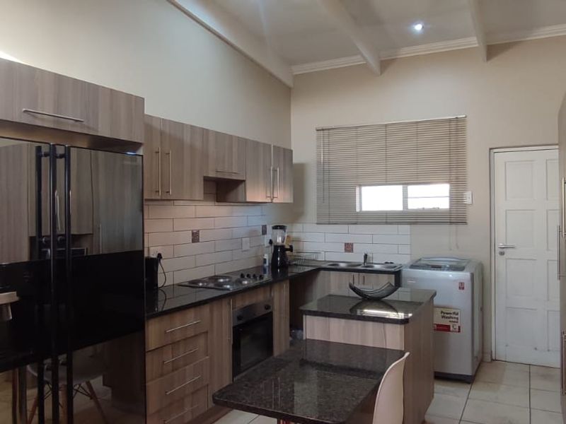 Modern kitchen featuring wood-finish cabinetry, granite countertops, integrated appliances, tiled backsplash, and exposed ceiling beams.