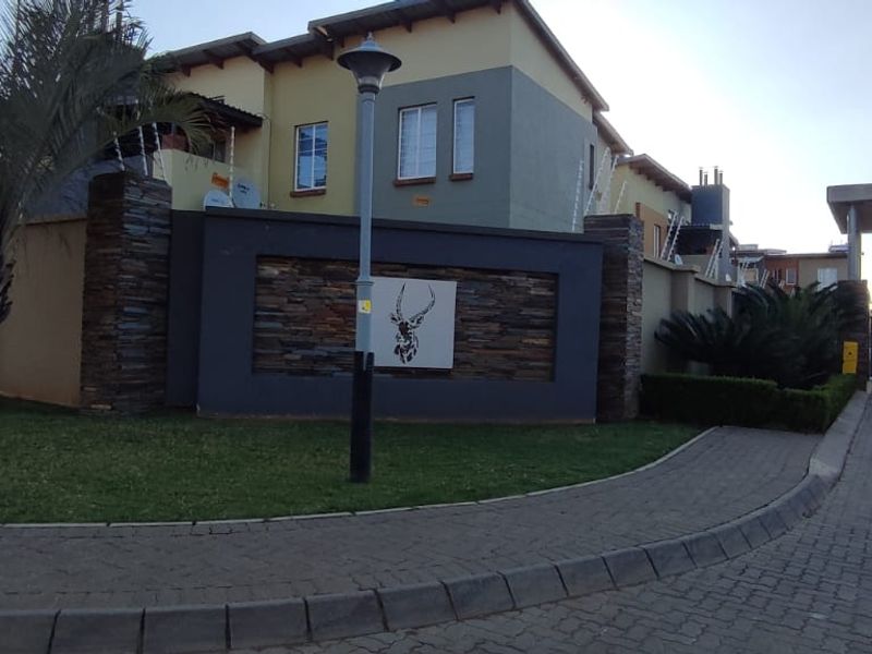 Front entrance view of the townhouse complex featuring a stone-clad feature wall, paved driveway, and secure gated access.