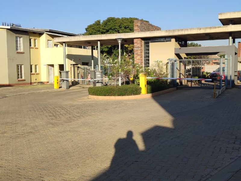 The entrance to the townhouse complex features a paved driveway, security boom gate, and a guard house structure.