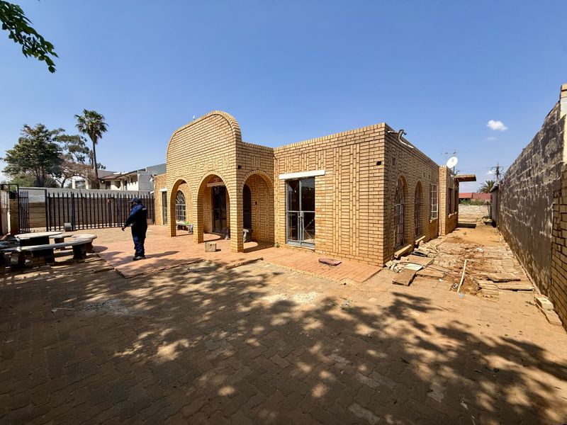 Rear exterior view of a face brick house featuring arched architectural details, a paved patio area, and secure boundary walling.