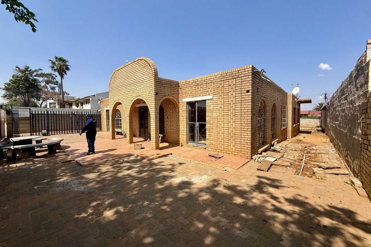 Rear exterior view of a face brick house featuring arched architectural details, a paved patio area, and secure boundary walling.