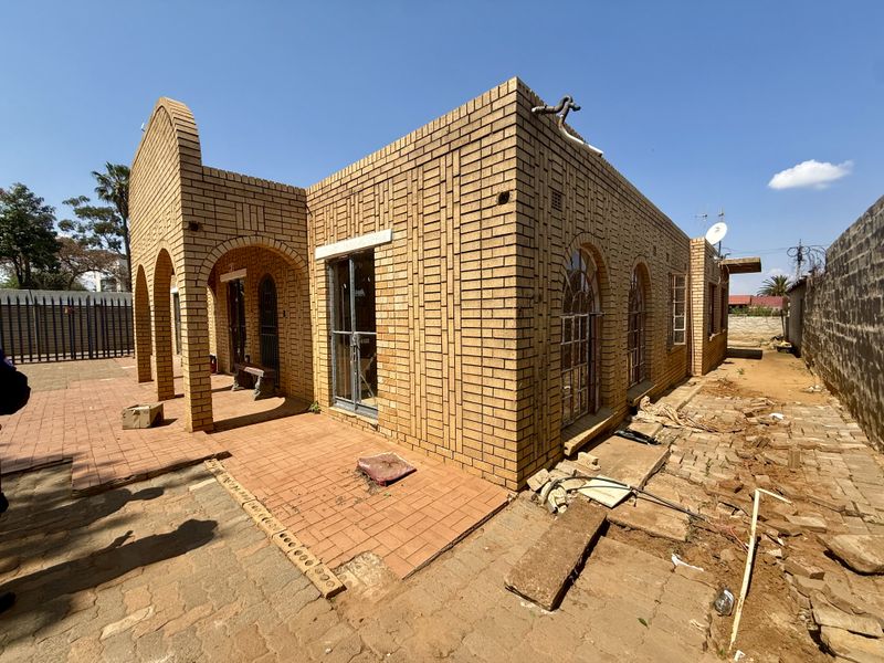 Rear view of a face brick house featuring an arched portico, paved patio area, and arched window frames, requiring exterior landscaping and maintenance.