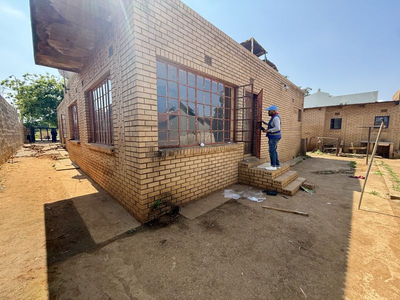 Rear view of a face brick house featuring steel window frames and a concrete slab roof, showing signs of wear and maintenance requirements.