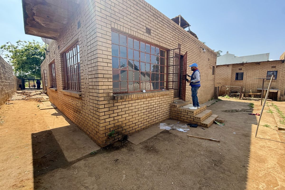 Rear view of a face brick house featuring steel window frames and a concrete slab roof, showing signs of wear and maintenance requirements.