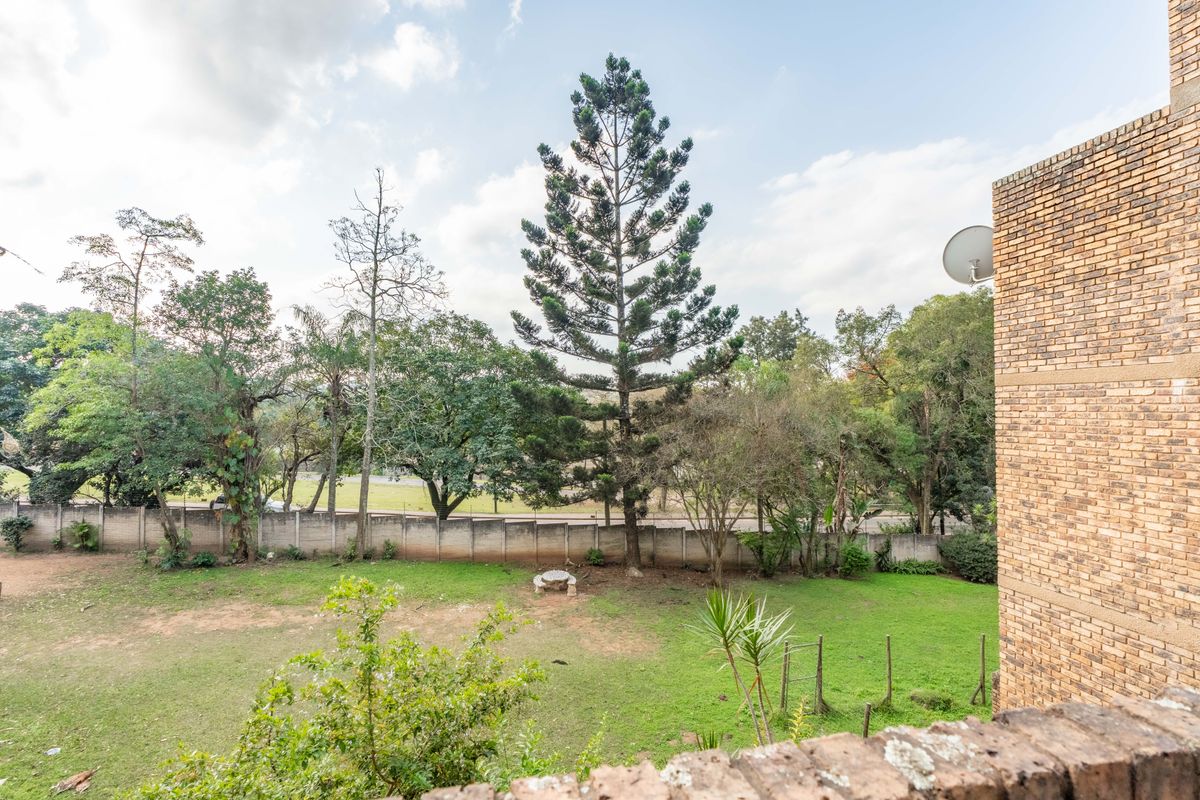 View of the rear garden area featuring a large lawn, mature trees, and a boundary wall, viewed from an elevated brick balcony.