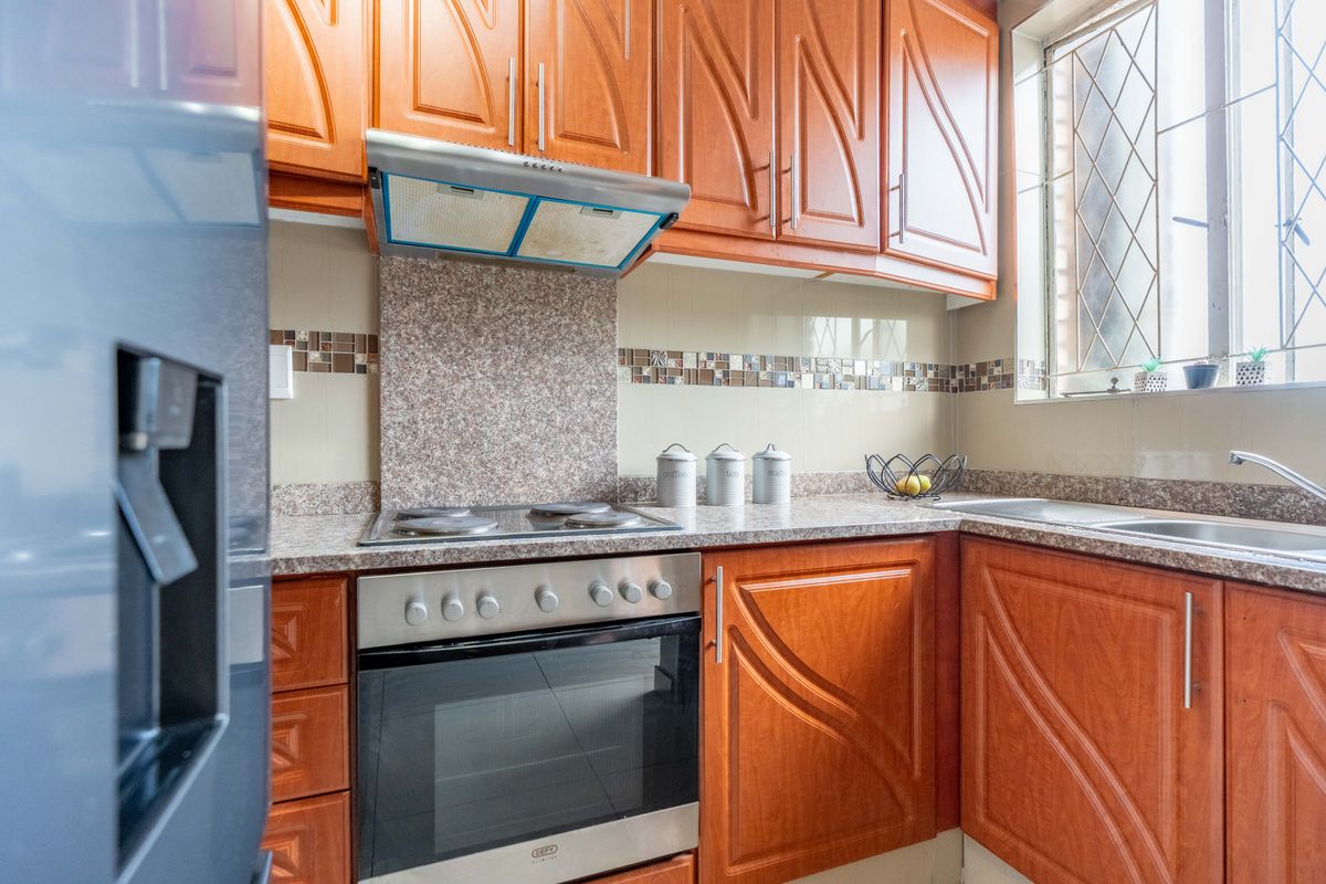 A functional kitchen featuring wooden cabinetry, granite countertops, a built-in oven with hob, and a tiled backsplash with a window for natural light.