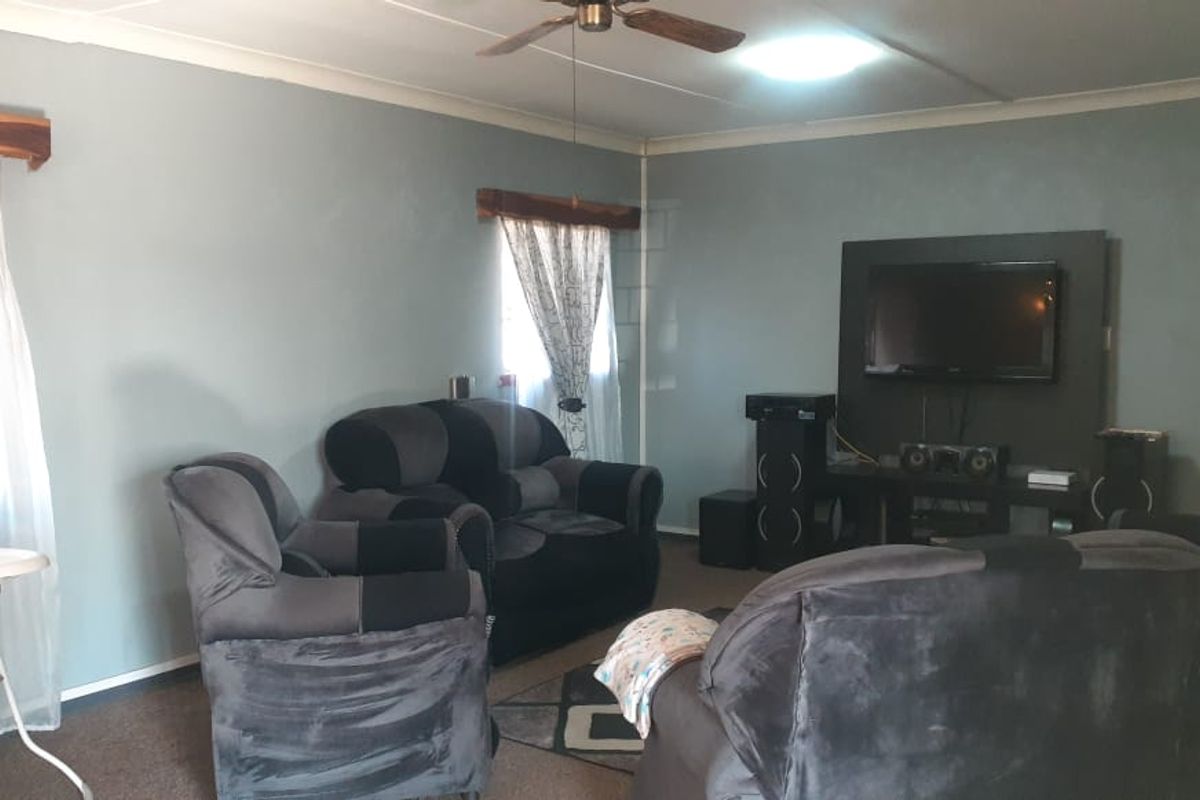 A living room featuring a ceiling fan, built-in television wall panel, and carpeted flooring.