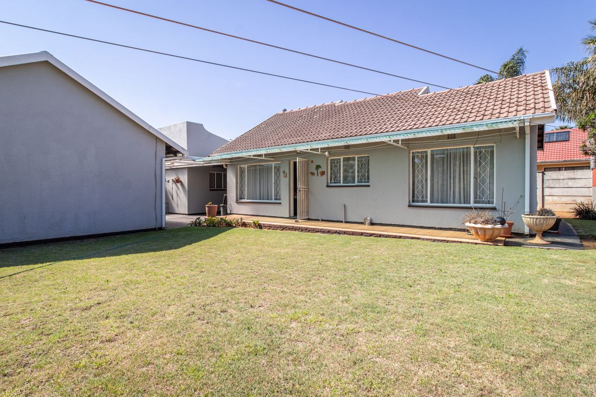 Rear view of the house featuring a tiled roof, security-fitted windows, and a paved walkway leading to a well-maintained lawn area.