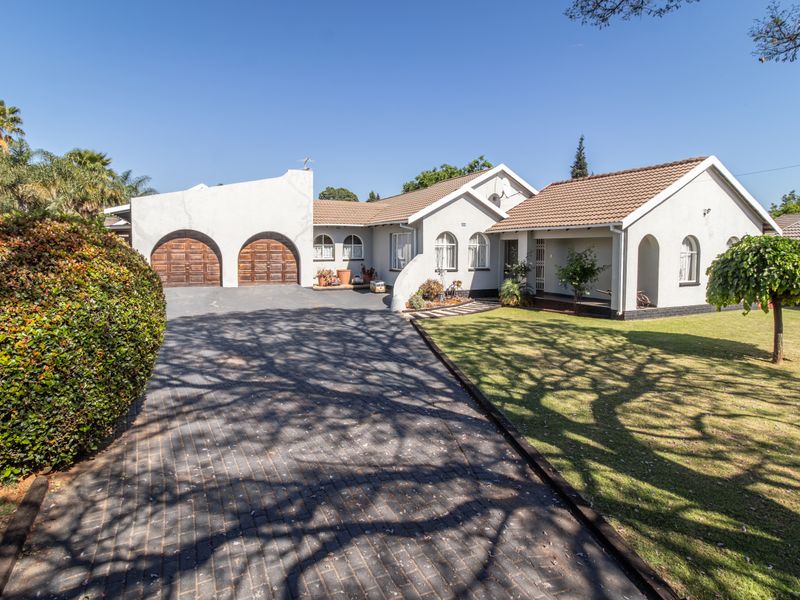 A well-maintained single-story family home featuring a paved driveway, double garage with arched doors, and a manicured front garden.