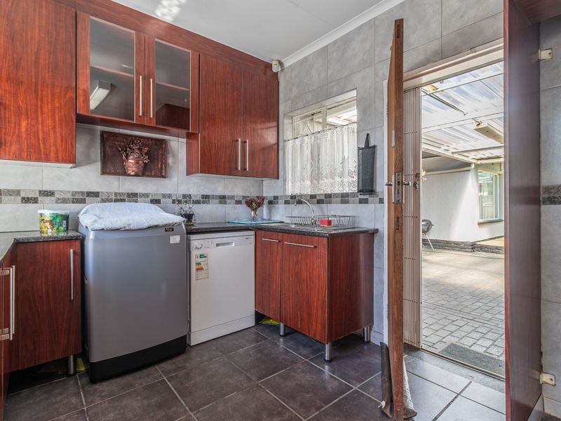 Functional scullery featuring wood-finish cabinetry, granite countertops, tiled backsplash, and direct access to the outdoor patio area.